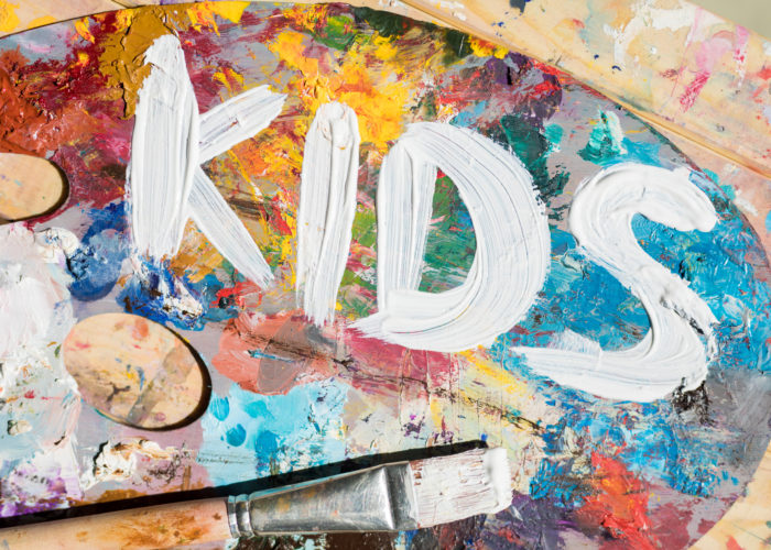Words kids painted with white gouache on palette of artist with mixture of colors