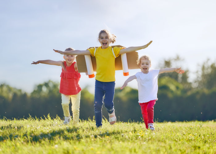 Little children playing astronaut. Girls fleeing and having fun in the park on sunset background. Kid in an astronaut costume dreaming of becoming a spaceman. Family games outdoors.
